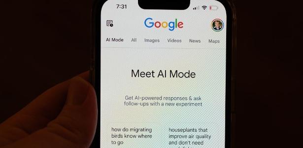 Pessoa segura tela de celular em que aparece o Modo IA (AI Mode, em inglês)