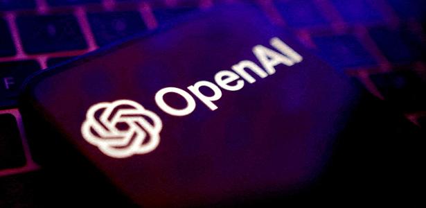 Logotipo da OpenAI, criadora do ChatGPT,  em tela de celular com teclado ao fundo