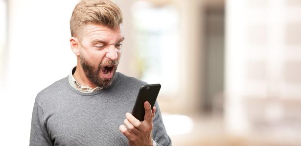 Homem com celular smartphone e expressão de raiva ódio nervoso
