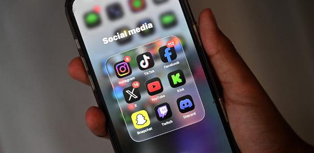 Tela de celular com pasta de ícones de redes sociais: Instagram, TikTok, Facebook, X, YouTube, Kick, Snapachat, Twitch e Discord